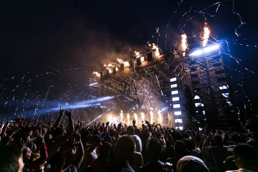 Concert crowd beneath bright festival stage lights — illustrative style reference