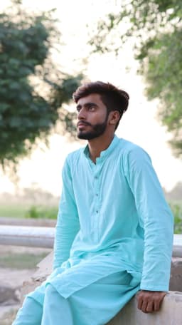 Man in a turquoise kurta seated on a low wall outdoors — illustrative style reference