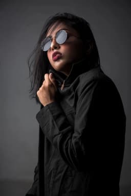 Woman wearing sunglasses and a black jacket against a dark background — illustrative style reference
