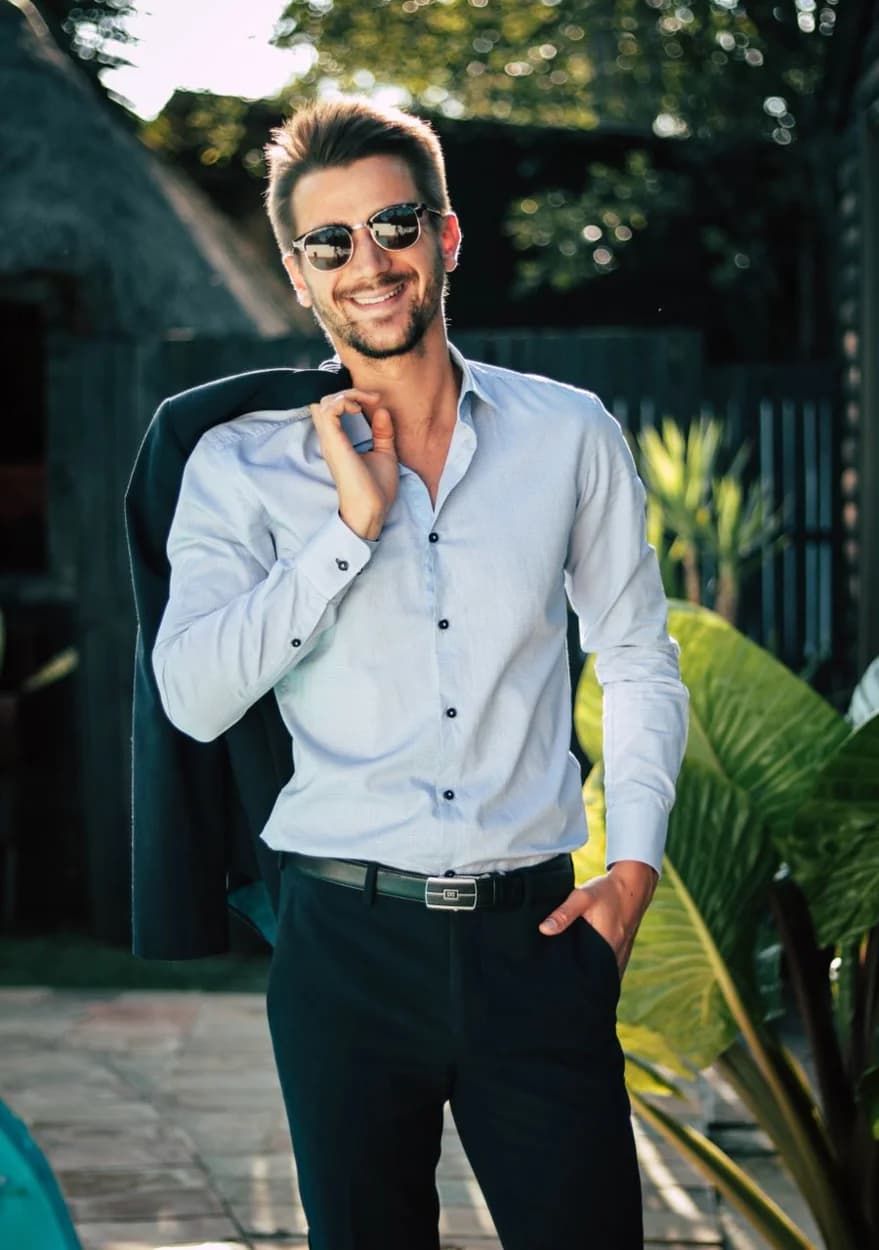 Man wearing sunglasses and a light blue shirt with a jacket over his shoulder — illustrative style reference