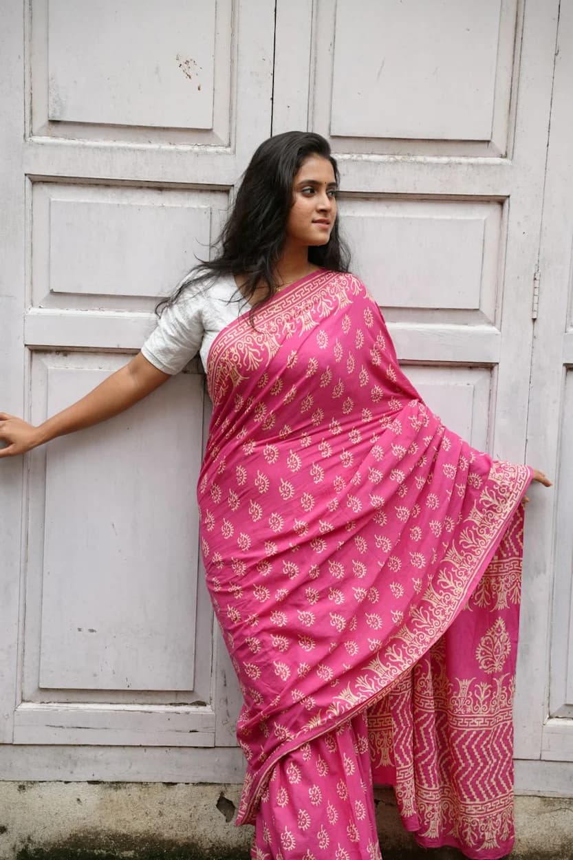 Woman in a bright pink saree standing beside paneled doors — illustrative style reference